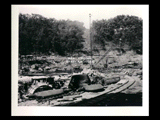 Dam and tunnel intake site during the hydroelectric power construction on the New River. Nine foot butterfly valves and casings for sluices shown in foreground and partially completed railway trestle over river at right. Faulconer Construction Company name on equipment. New-Kanawha Power Company, Hawks Nest - Gauley Junction Development No. 138.