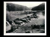 Dam during the hydroelectric power construction on the New River. Completed foundations for spillway portion of dam. Pier blocks concreted to floor of inspection tunnel. Buildings along the river in the distance. New-Kanawha Power Company, Hawks Nest - Gauley Junction Development No. 278.