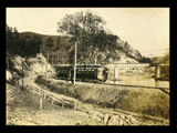 View of track near Annabelle with car No. 230 on track and bridge over river in background. Rural setting.